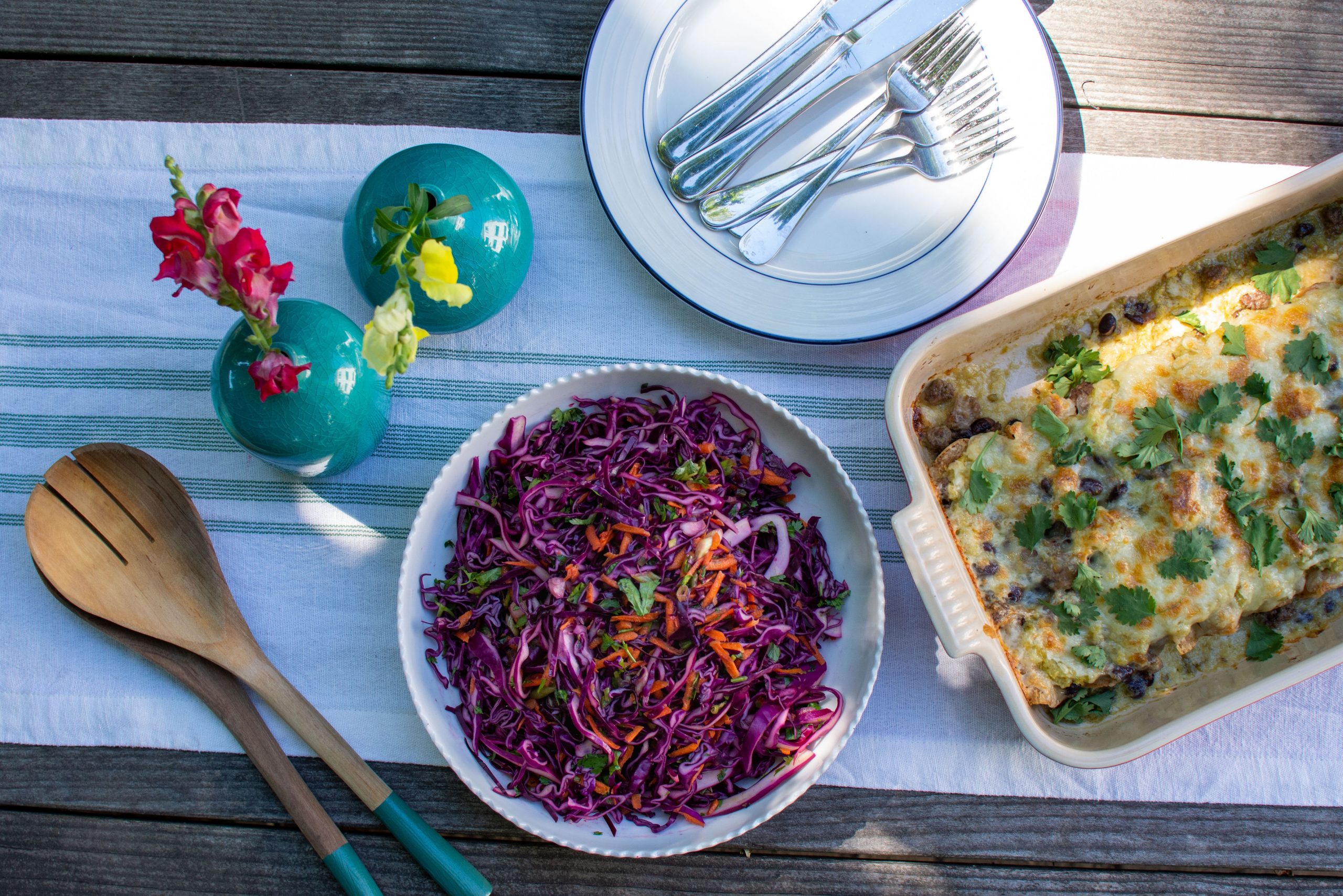 Photo of dinner set on table with beef enchiladas, purple slaw, and turquoise vases of flowers. Boston Area Meal Delivery Service.